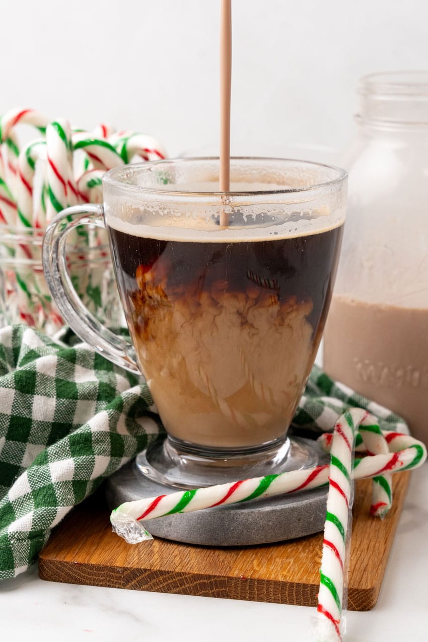 homemade peppermint bark coffee creamer being poured into a glass mug filled with black coffee