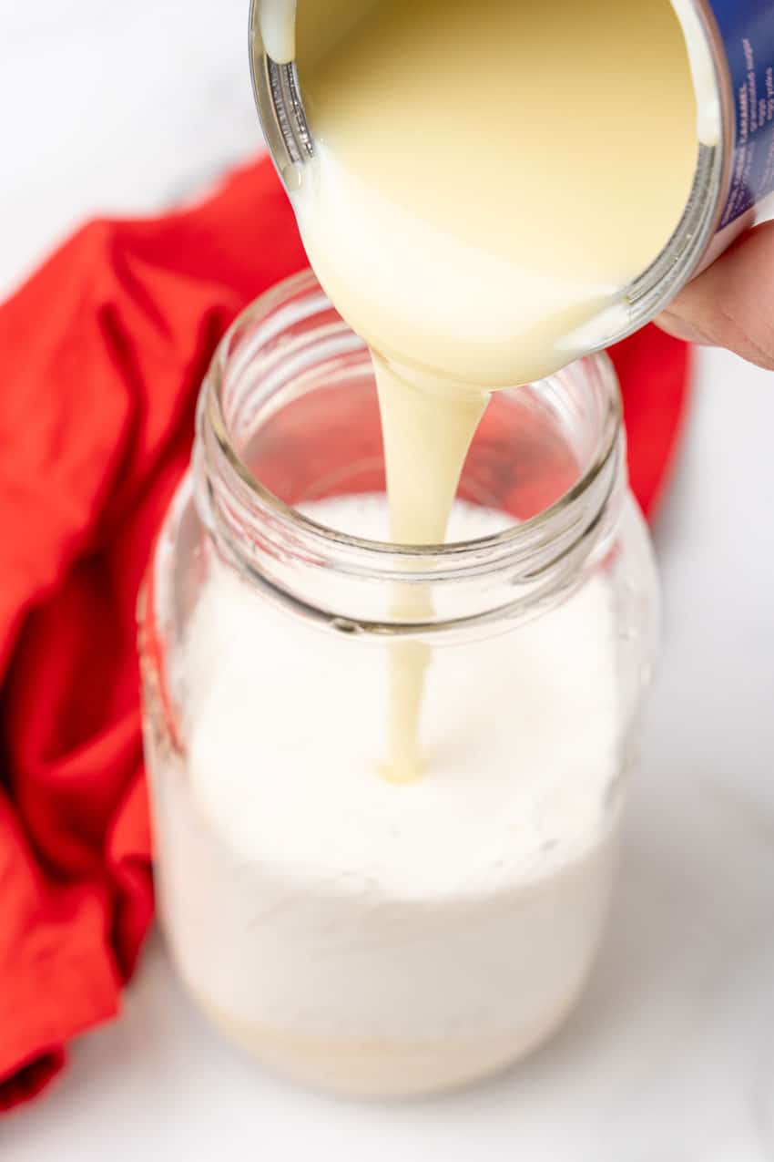 condensed milk being poured into a glass har filled with half and half