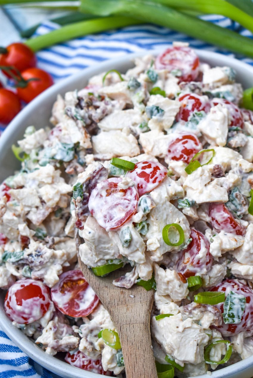 a wooden spoon scooping blt chicken salad out of a large white serving bowl