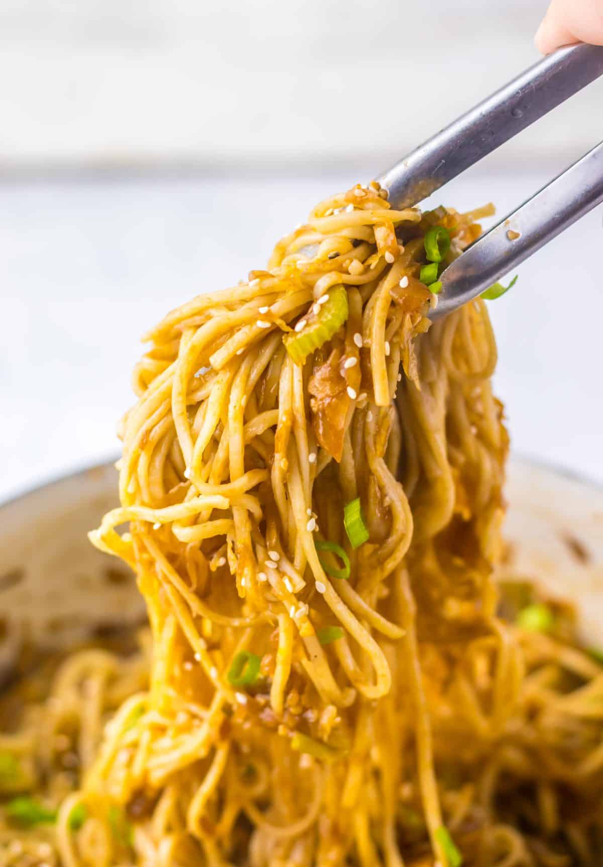 metal tongs pulling chinese chow mein noodles out of a pot