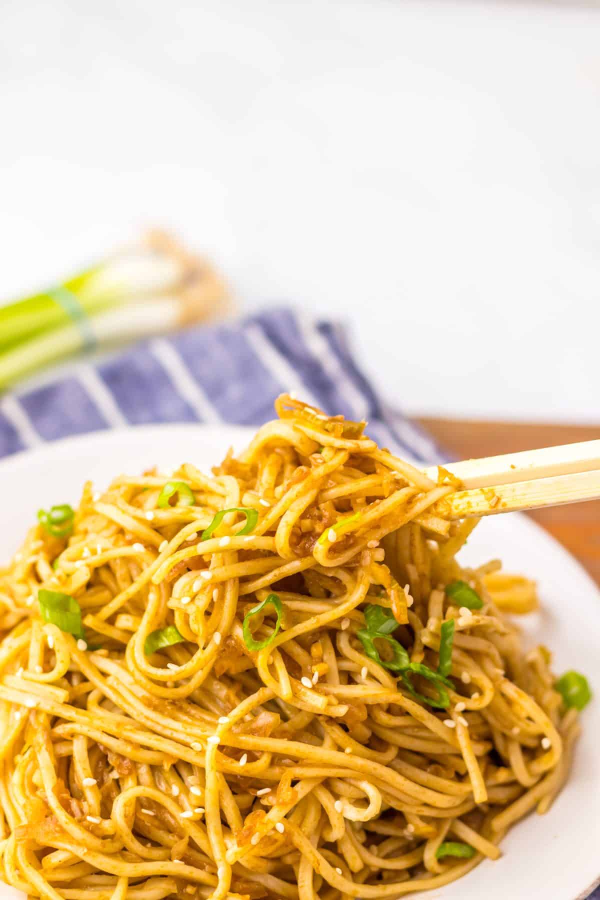 wooden chop sticks scooping chinese chow mein noodles off a white plate