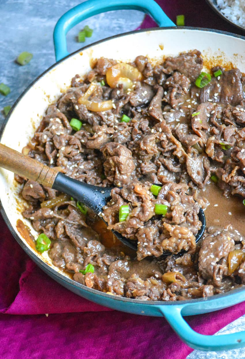 a wooden spoon scooping homemade beef bulgogi out of a large cast iron skillet
