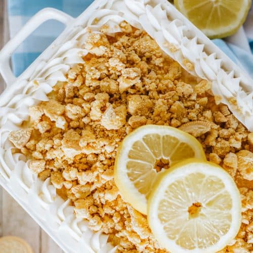 lemon oreo lasagna in a white casserole dish topped with crumbled oreo cookies and two slices of fresh lemon