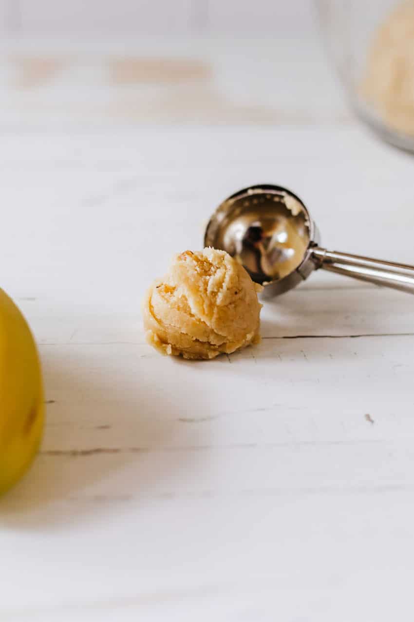 a cookie scoop dropping a ball of banana bread cake ball dough on a wooden table