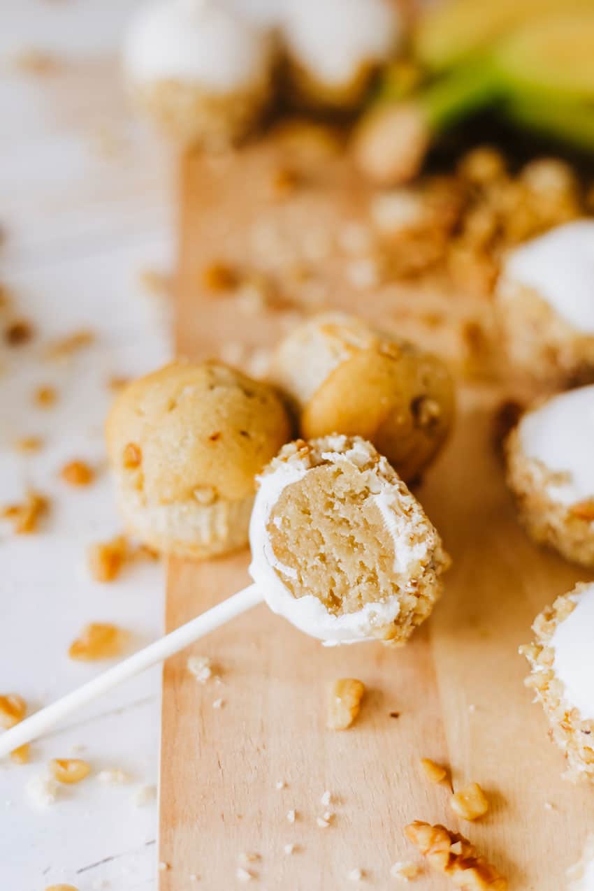 half of a banana bread cake pop resting on a wooden cutting board with walnut pieces