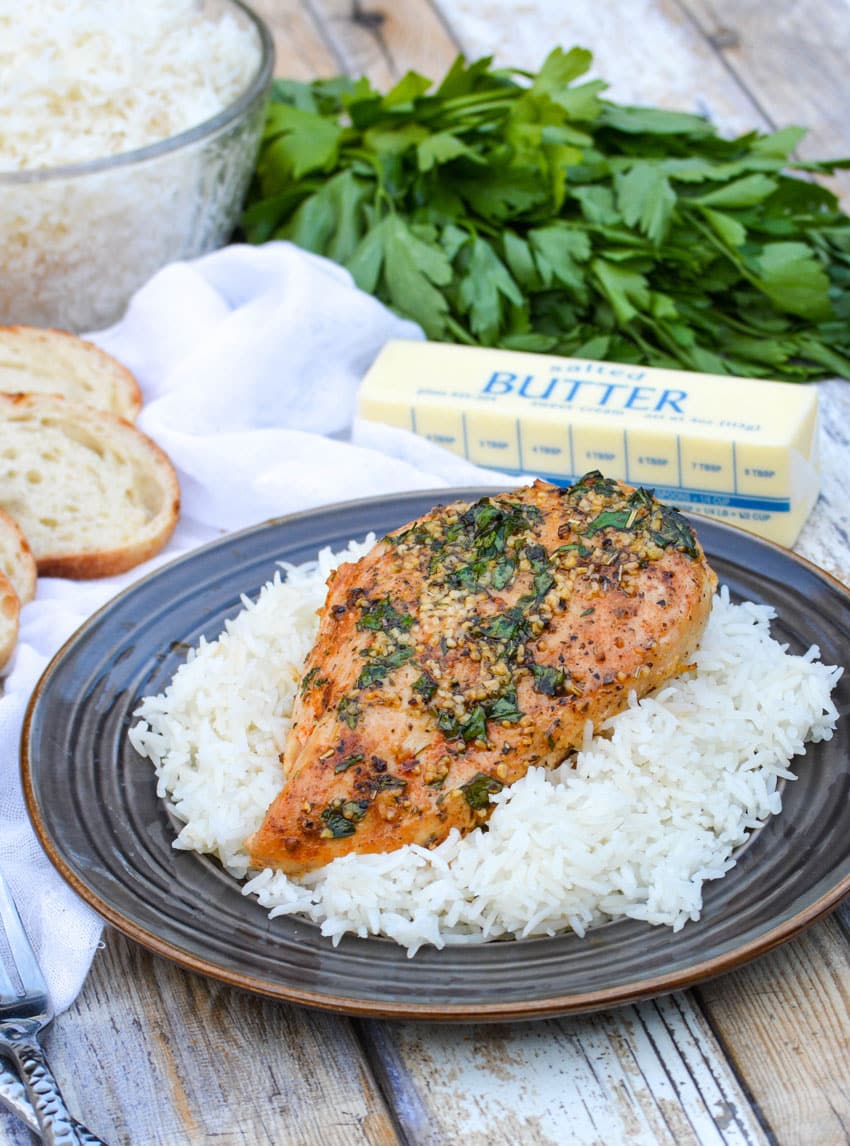a baked garlic butter chicken breast resting on steamed white rice on a brown plate
