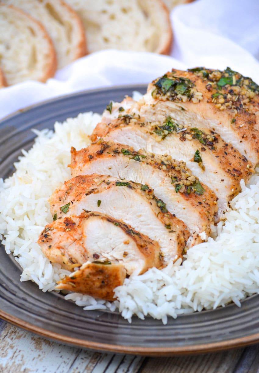 a sliced baked garlic butter chicken breast resting on steamed white rice on a brown plate