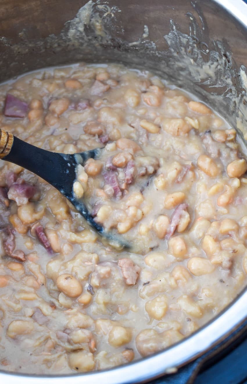 a black spoon scooping ham and beans out of an instant pot