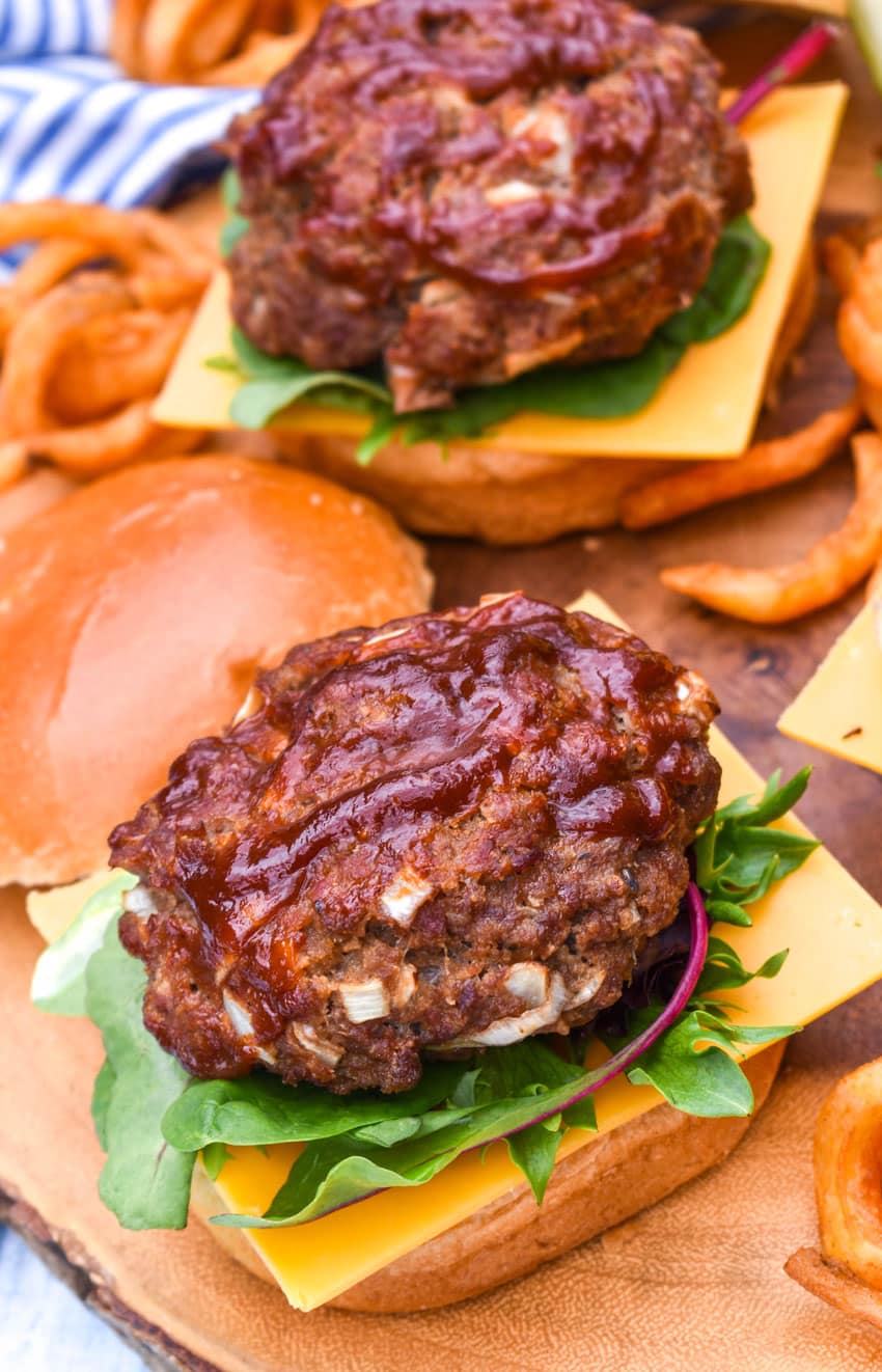 meatloaf burgers on a wooden cutting board with dill pickle spears in the background