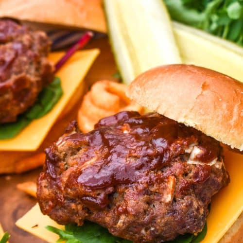 meatloaf burgers on a wooden cutting board with dill pickle spears in the background