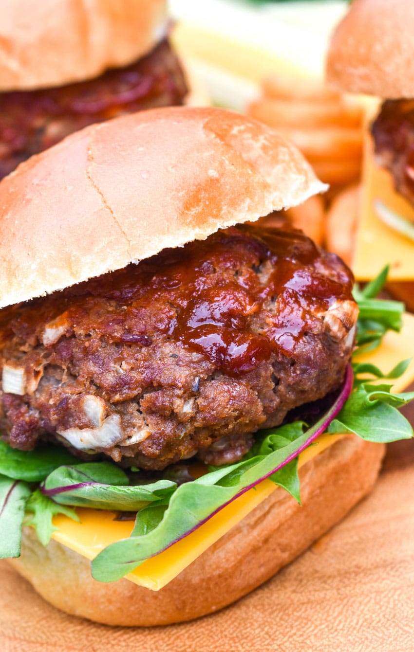 meatloaf burgers on a wooden cutting board with dill pickle spears and crispy curly fries in the background
