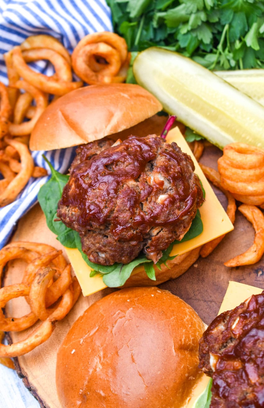 meatloaf burgers on a wooden cutting board with dill pickle spears and crispy curly fries in the background