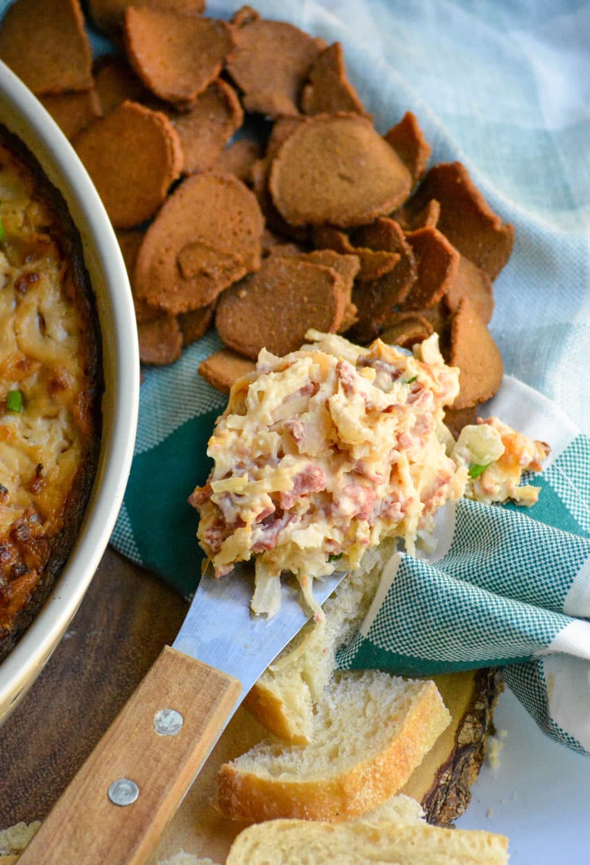 a cheese spreader holding a scoop of baked reuben dip resting on a cloth napkin