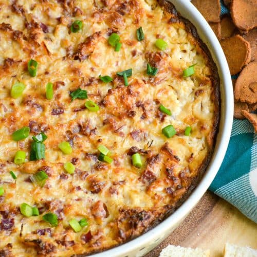 baked reuben dip topped with sliced green onions in a ceramic baking dish