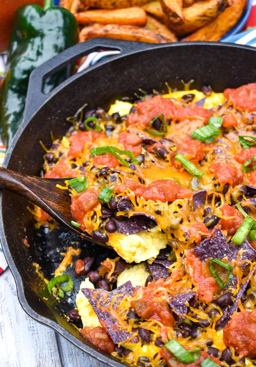 a wooden spatula scooping a southwestern breakfast scramble out of a large black cast iron skillet