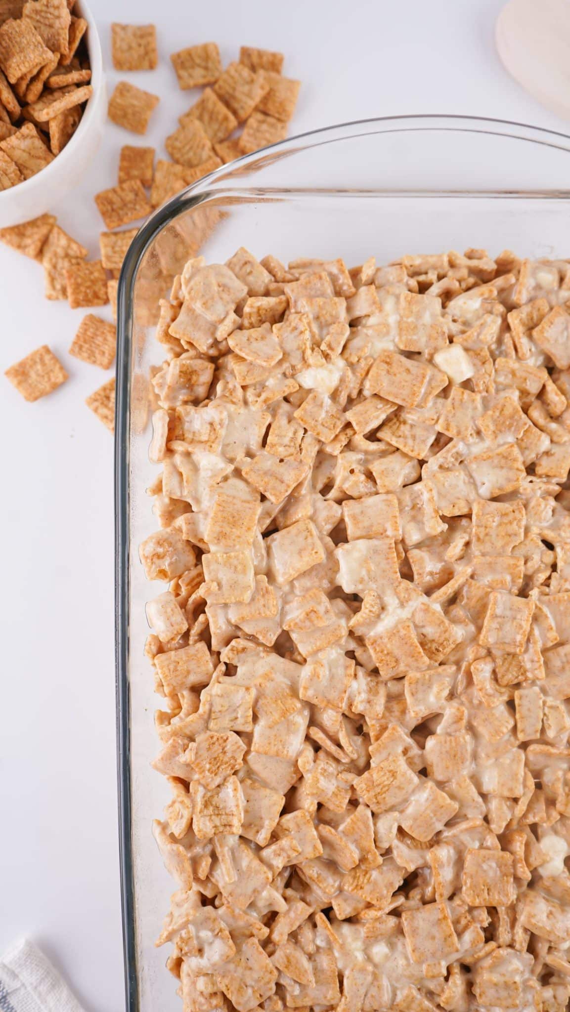 marshmallow coated cinnamon toast crunch cereal spread out in a large glass baking dish