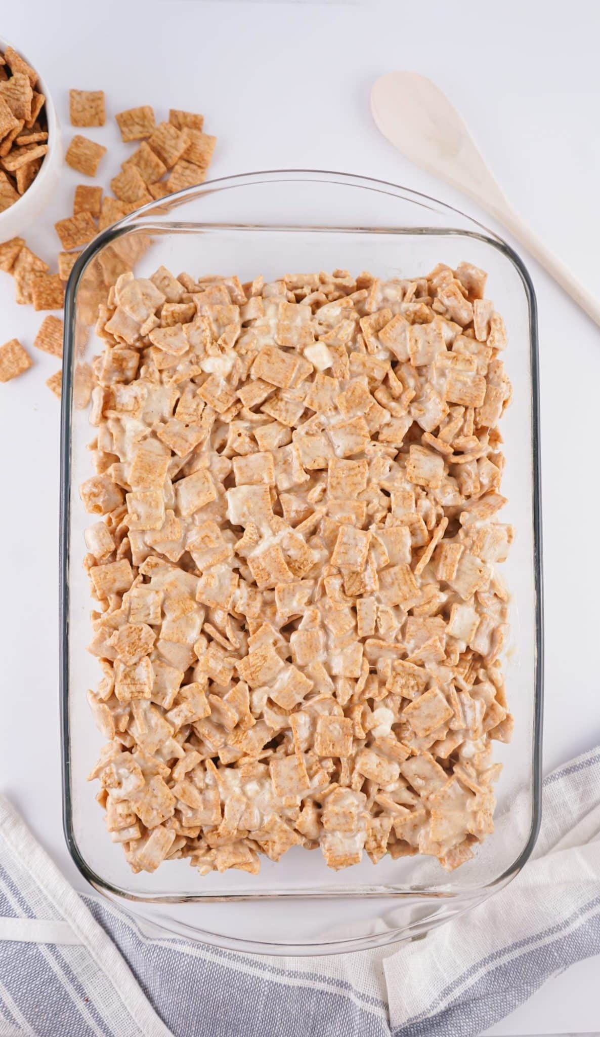 marshmallow coated cinnamon toast crunch cereal spread out in a large glass baking dish