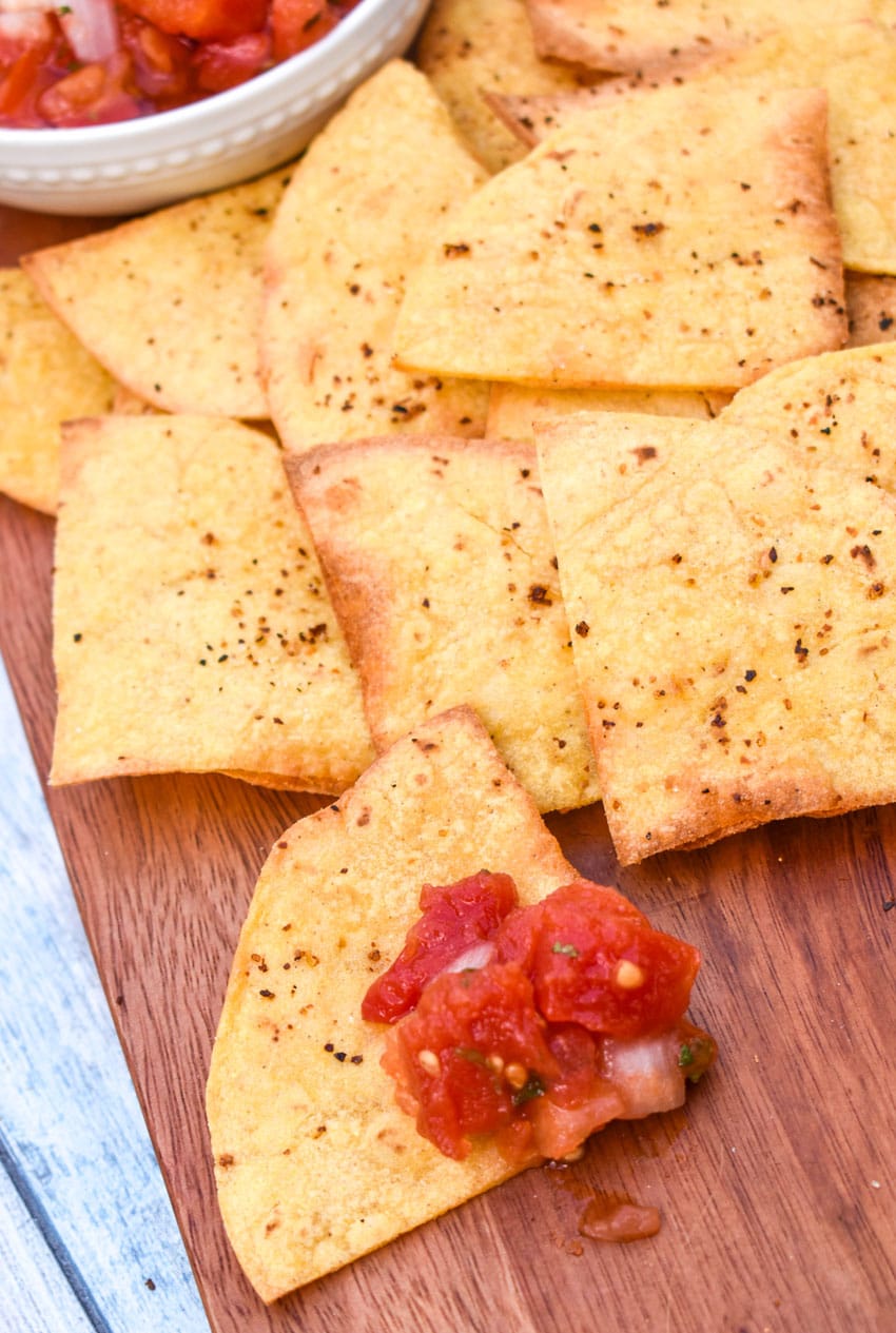 air fryer tortilla chops on a wooden cutting board with a bowl of salsa on the side
