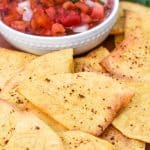 air fryer tortilla chops on a wooden cutting board with a bowl of salsa on the side