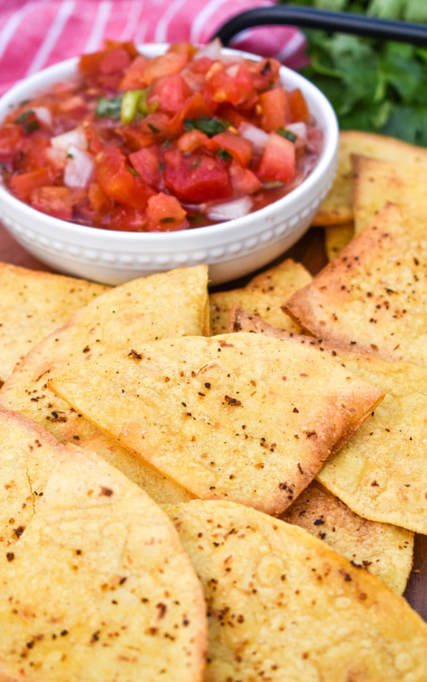 air fryer tortilla chops on a wooden cutting board with a bowl of salsa on the side
