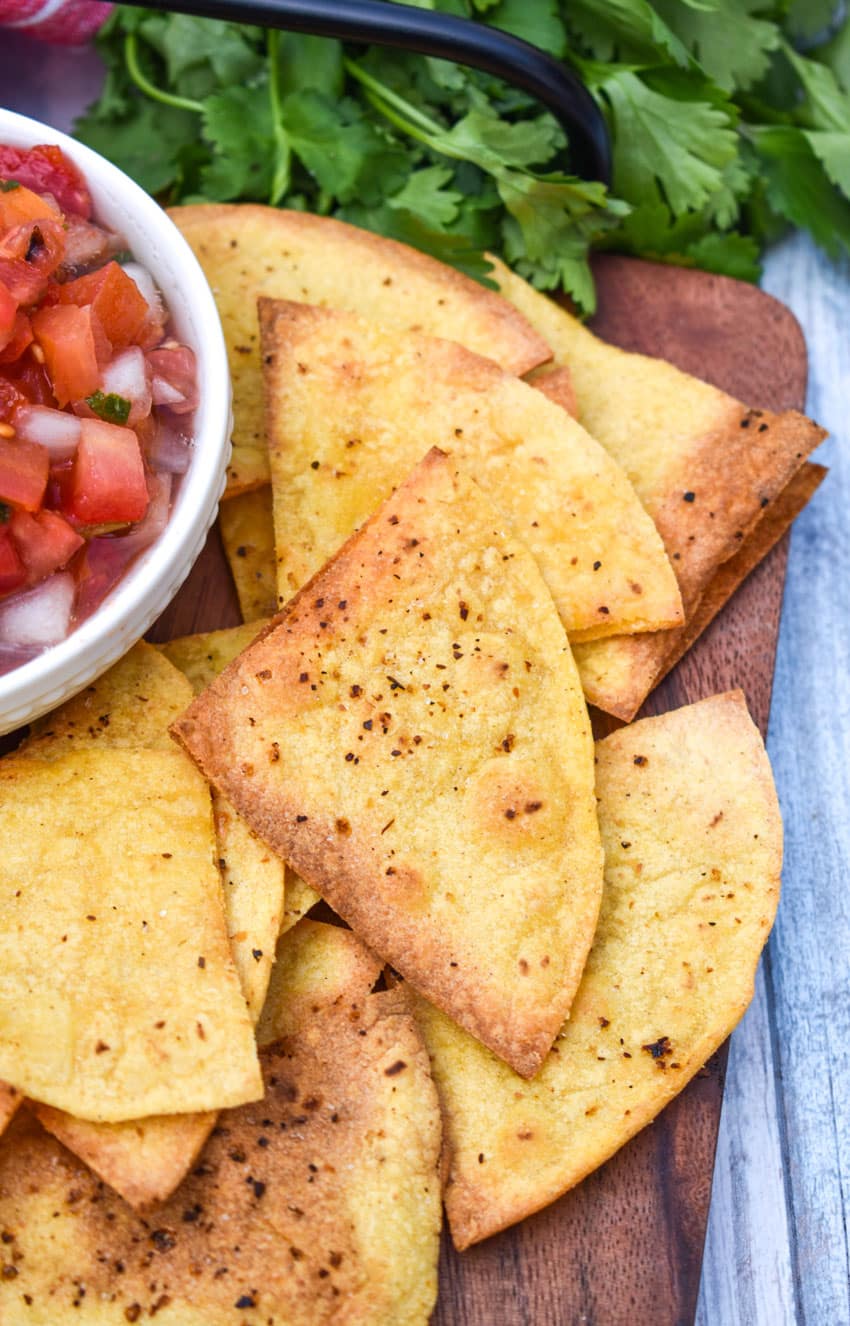 air fryer tortilla chops on a wooden cutting board with a bowl of salsa on the side