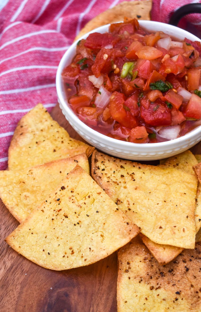 air fryer tortilla chops on a wooden cutting board with a bowl of salsa on the side