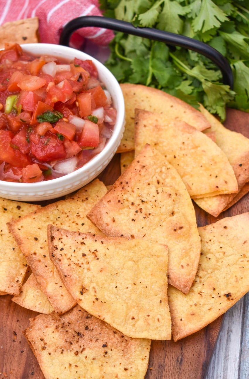 air fryer tortilla chops on a wooden cutting board with a bowl of salsa on the side