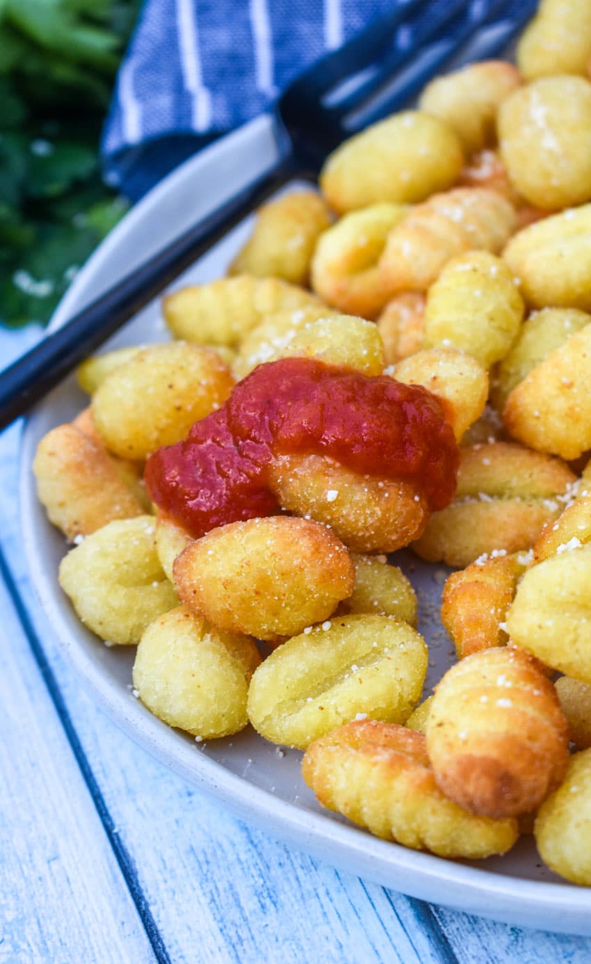 crispy air fryer gnocchi on a large white plate with a small bowl of marinara sauce on the side