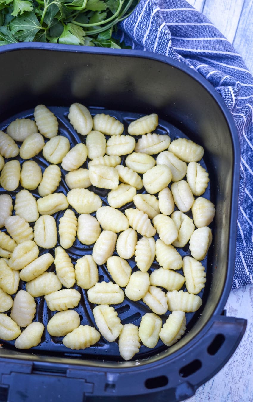 olive oil coated potato gnocchi spread out in an even layer in the basket of an air fryer