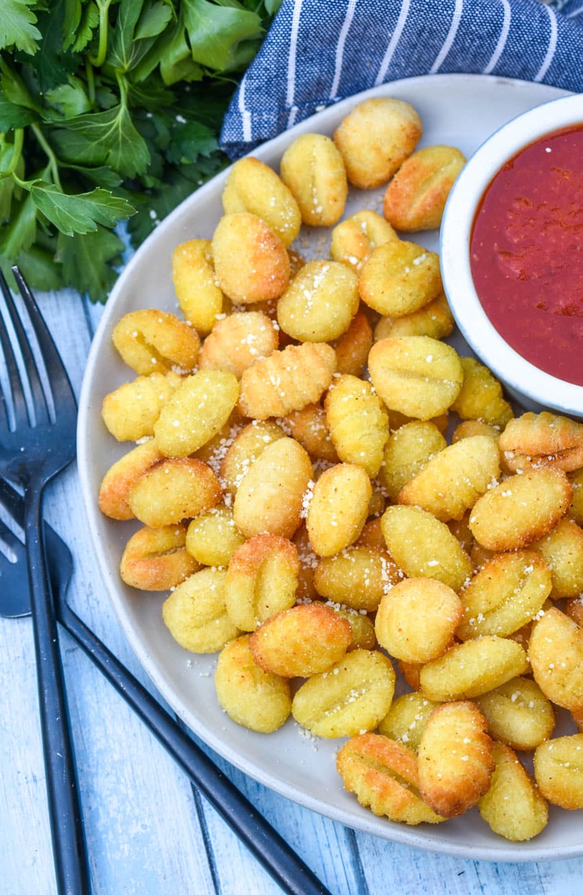 crispy air fryer gnocchi on a large white plate with a small bowl of marinara sauce on the side