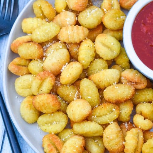 crispy air fryer gnocchi on a large white plate with a small bowl of marinara sauce on the side