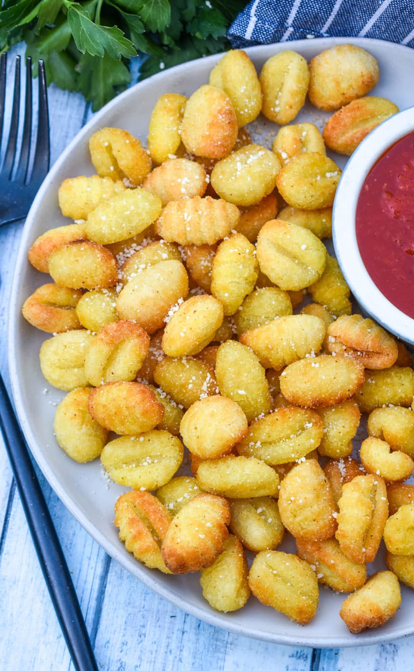 Crispy Air Fryer Gnocchi crispy air fryer gnocchi on a large white plate with a small bowl of marinara sauce on the side