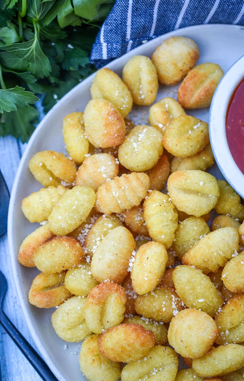 crispy air fryer gnocchi on a large white plate with a small bowl of marinara sauce on the side