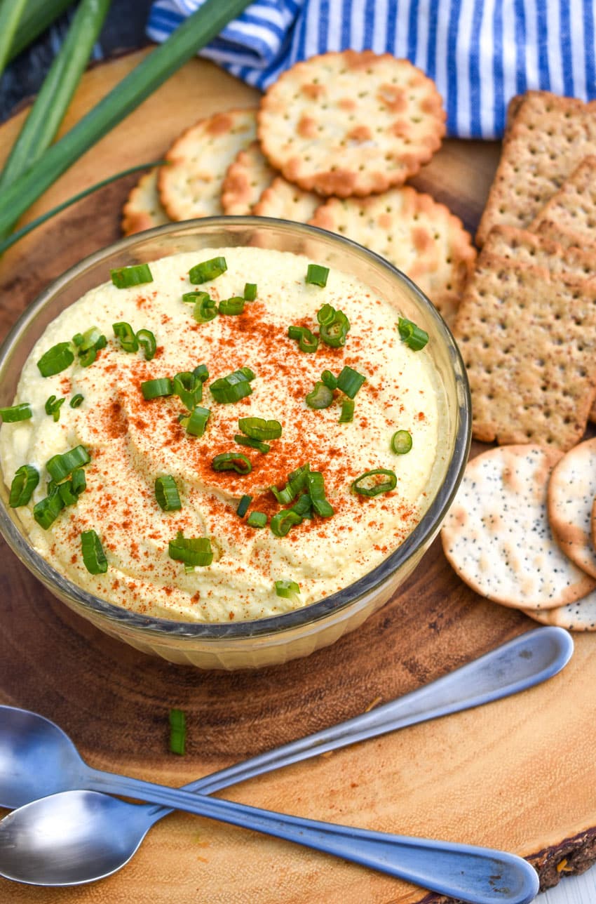 DEVILED EGG DIP TOPPED WITH SLICED GREEN ONIONS IN A SMALL GLASS BOWL
