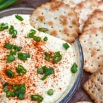 A CRACKER SCOOPING DEVILED EGG DIP OUT OF A SMALL GLASS BOWL