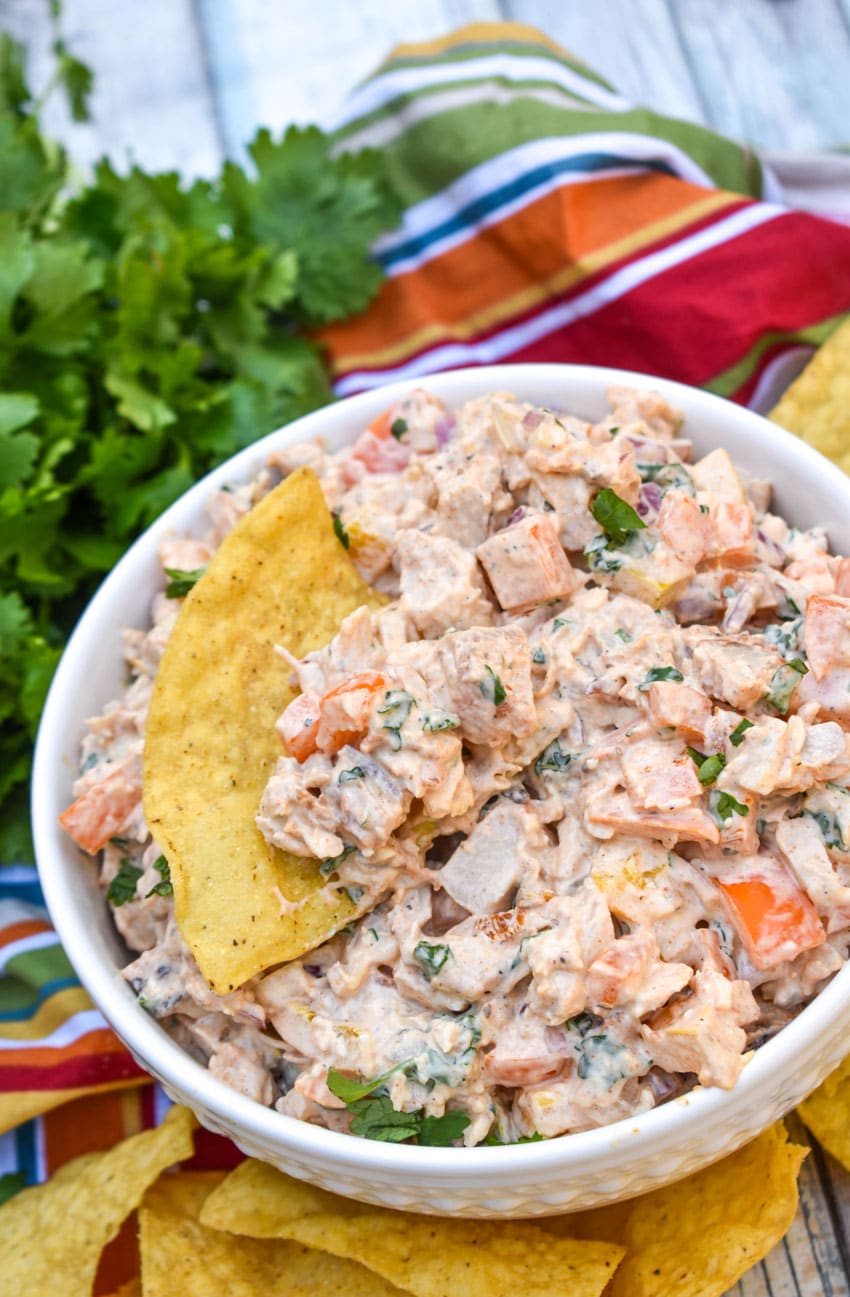 a corn tortilla chip scooping fajita chicken salad out of a white bowl