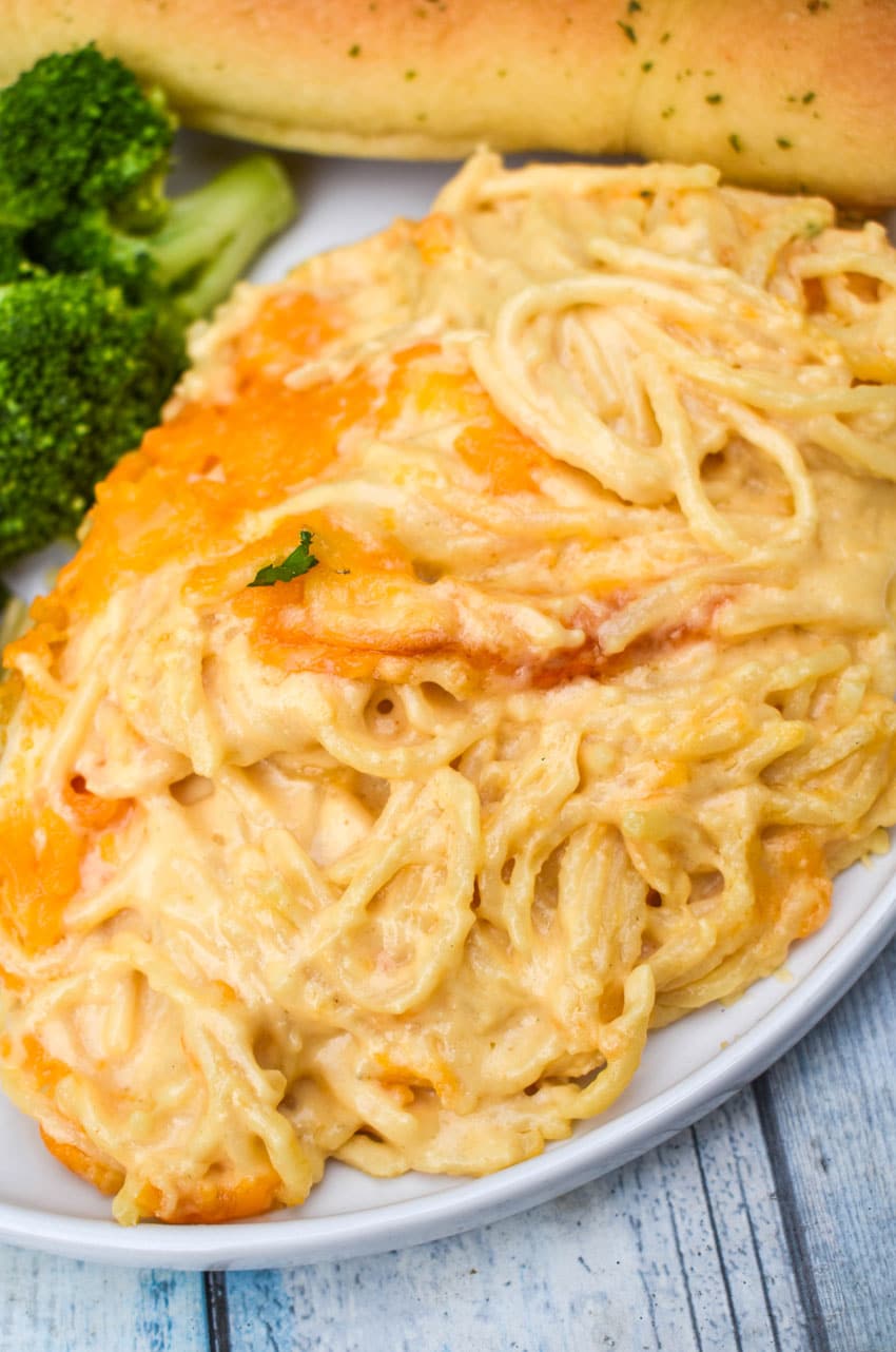spaghetti mac and cheese on a white plate with a fresh breadstick on the side