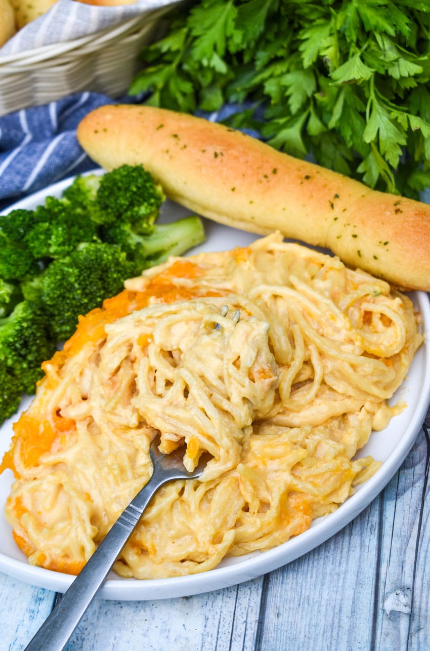 a silver fork scooping baked spaghetti mac and cheese off a white dinner plate
