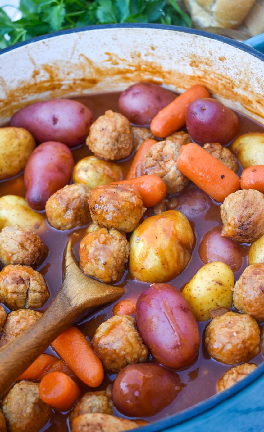 a wooden spoon scooping meatball pot roast out of a large blue dutch oven