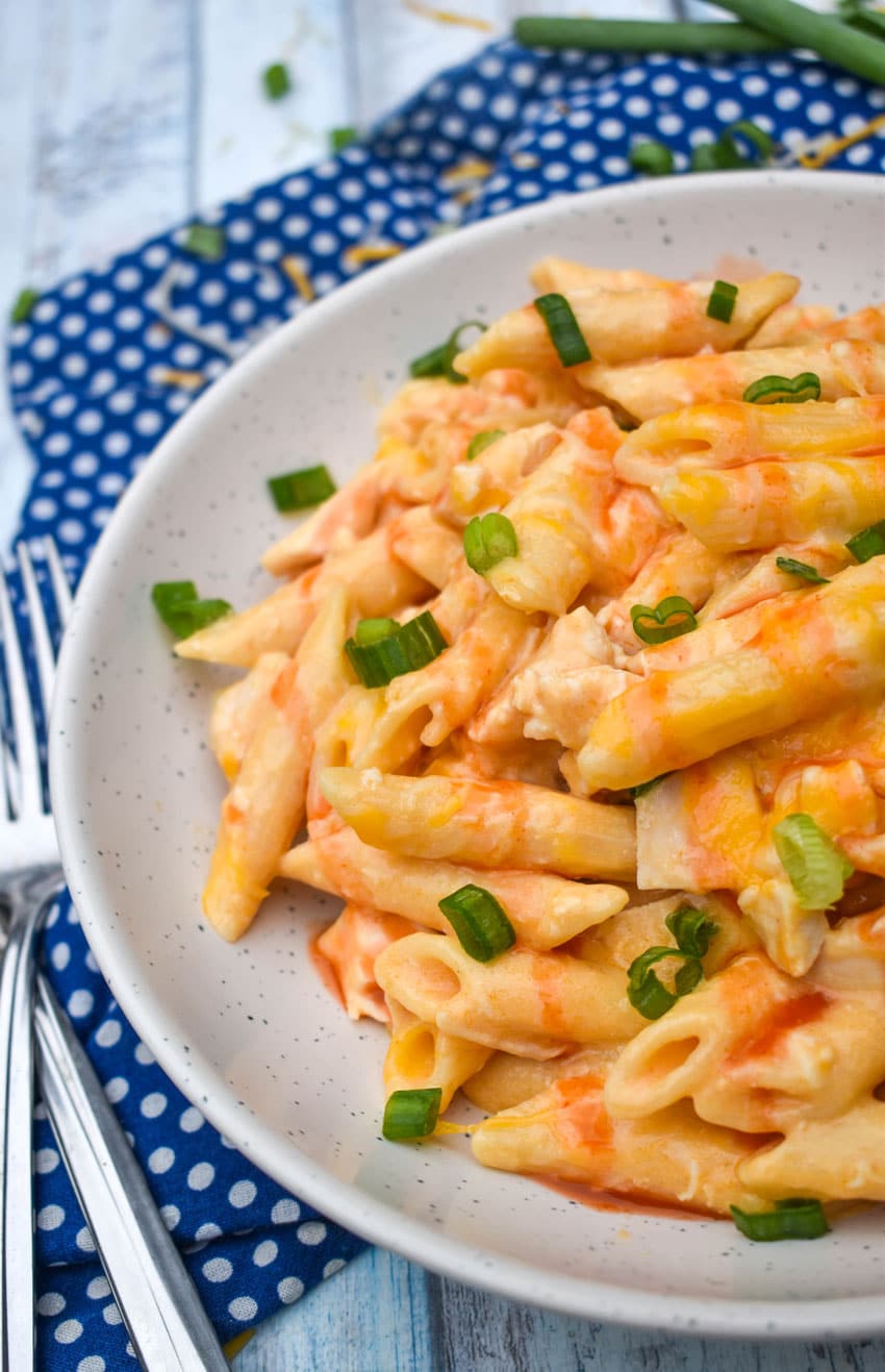 ONE POT CREAMY BUFFALO CHICKEN PASTA TOPPED WITH SLICED GREEN ONIONS AND BUFFALO SAUCE ON A SMALL WHITE PLATE
