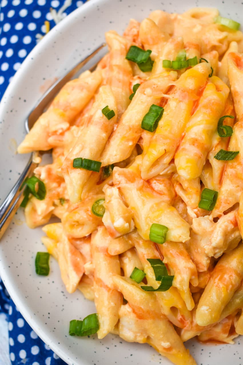 ONE POT CREAMY BUFFALO CHICKEN PASTA TOPPED WITH SLICED GREEN ONIONS AND BUFFALO SAUCE ON A SMALL WHITE PLATE