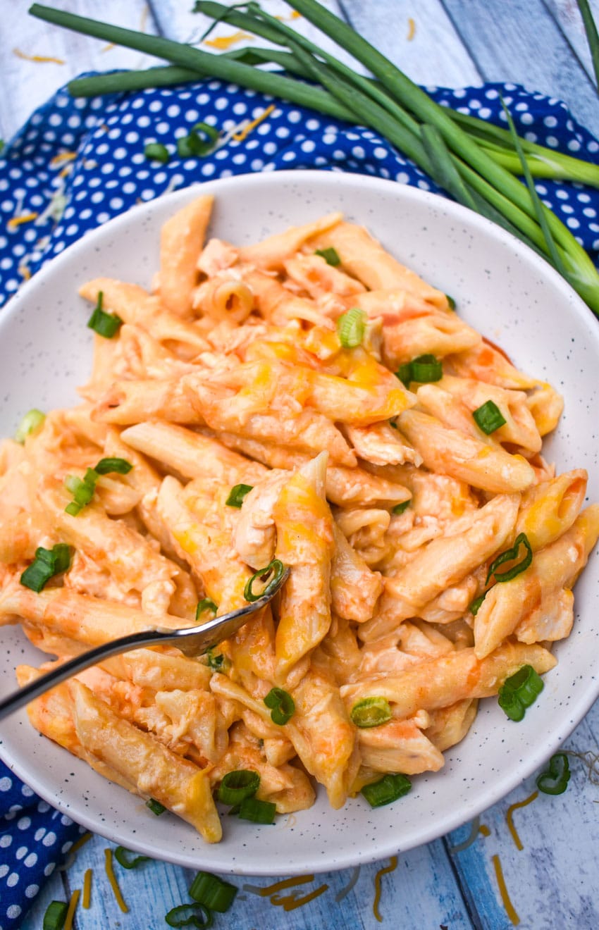 ONE POT CREAMY BUFFALO CHICKEN PASTA TOPPED WITH SLICED GREEN ONIONS AND BUFFALO SAUCE ON A SMALL WHITE PLATE
