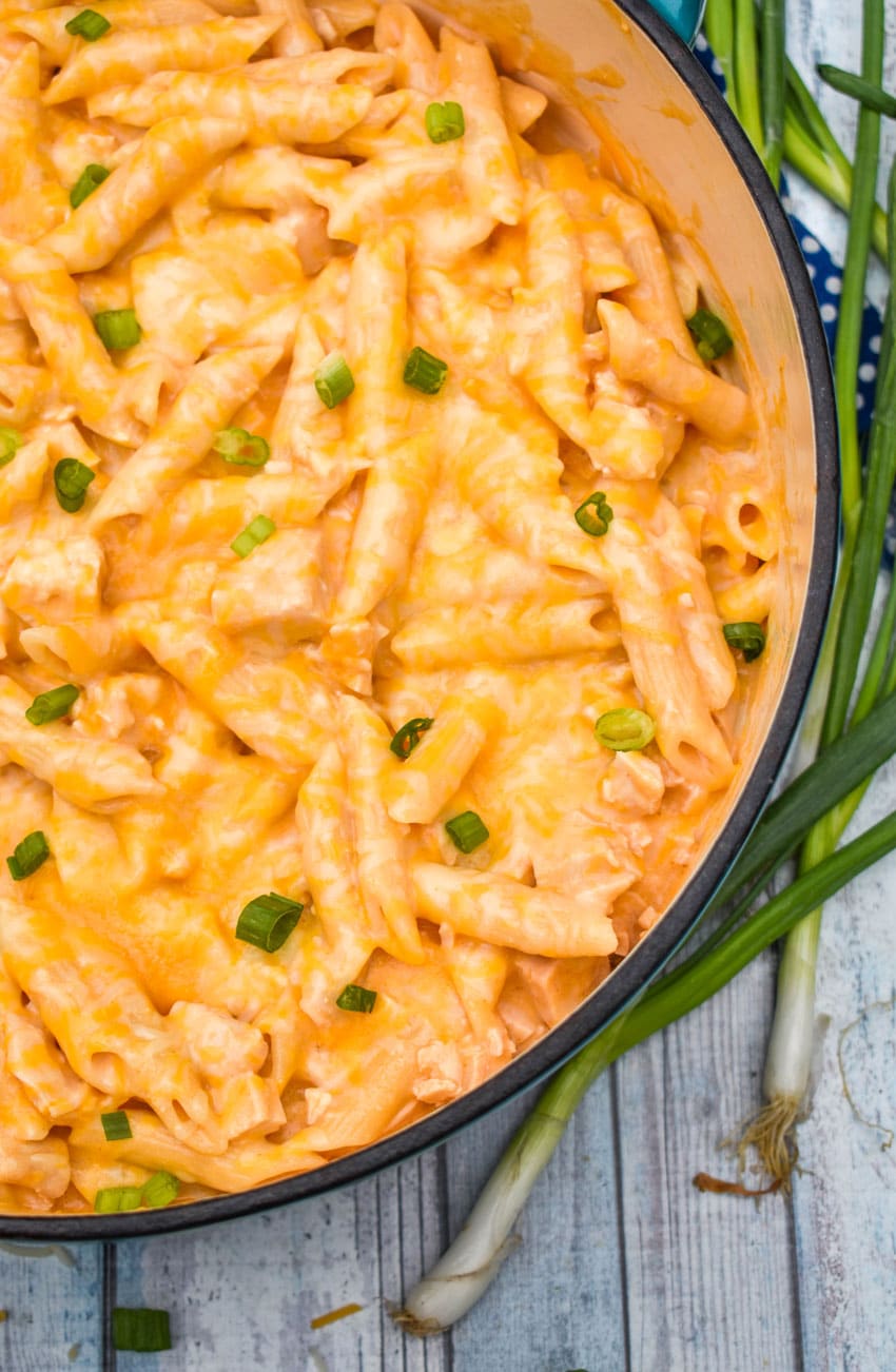 CREAMY BUFFALO CHICKEN PASTA TOPPED WITH SLICED GREEN ONIONS IN A LARGE BLUE DUTCH OVEN