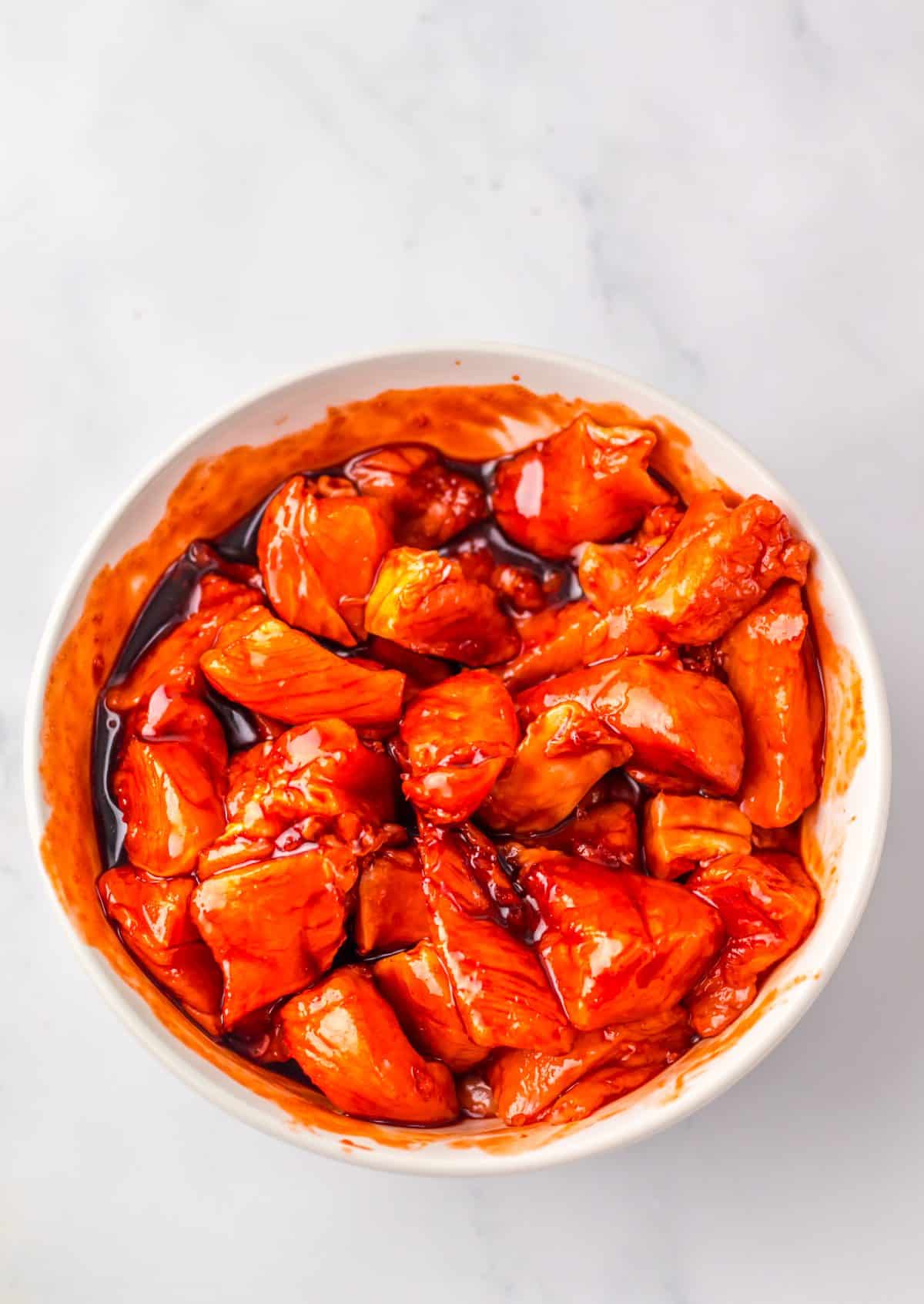 chunks of chicken marinading in asian sauce in a small white mixing bowl
