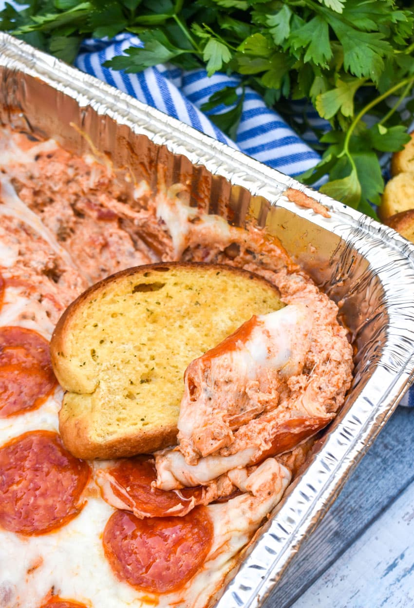 garlic texas toast scooping smoked pepperoni pizza dip out of an aluminum baking dish