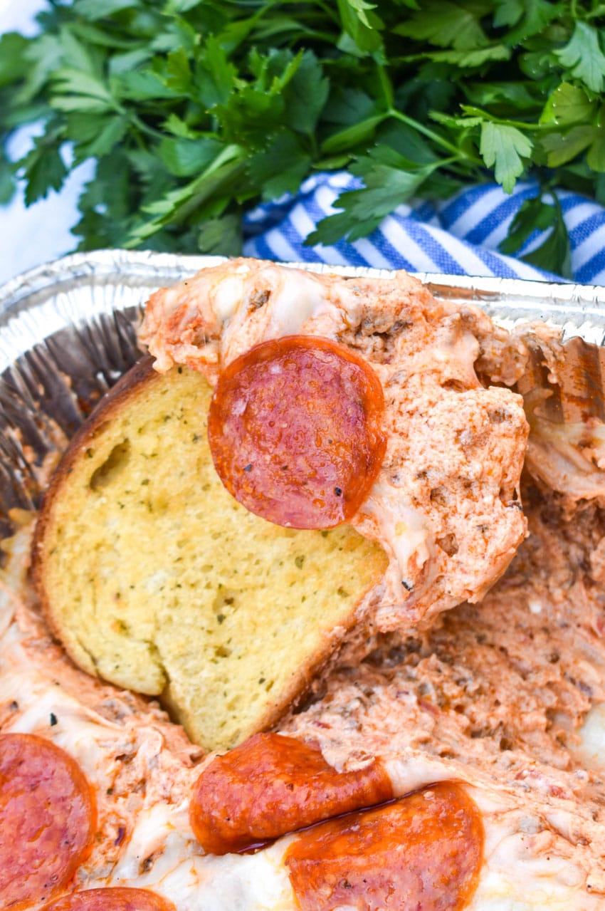 garlic texas toast scooping smoked pepperoni pizza dip out of an aluminum baking dish