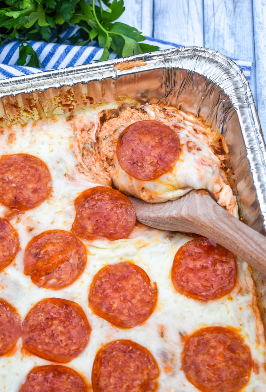 a wooden spoon scooping smoked pepperoni pizza dip out an aluminum pan