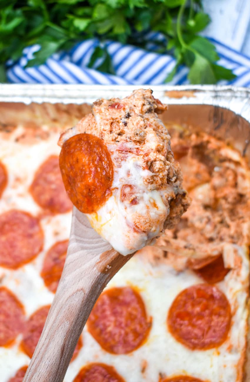 a wooden spoon holding up a scoop of smoked pepperoni pizza dip
