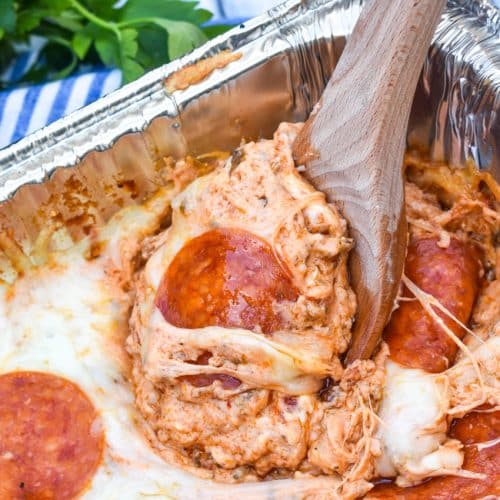 a wooden spoon scooping smoked pepperoni pizza dip out an aluminum pan