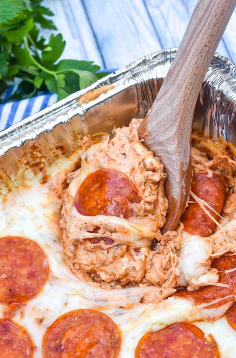 a wooden spoon scooping smoked pepperoni pizza dip out an aluminum pan